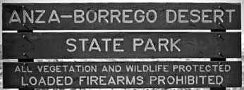 B/W photo of sign stating: 'ANZA-BERREGO DESERT STATE PARK / ALL VEGETATION AND WILDLIFE PROTECTED / LOADED FIREARMS PROHIBITED'
