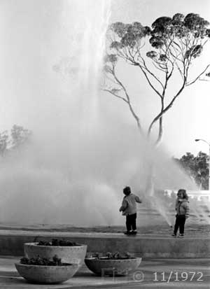 B/W photo: Two animated children at edge of large water fountain - Embedded text: 11/1972