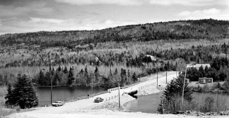 grayscale photograph: elevated view of gravel road and bridge over river