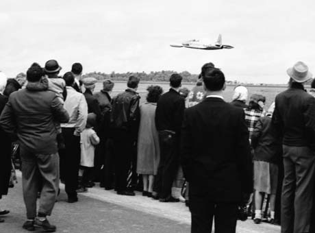 grayscale photograph: jet flying by airshow viewers