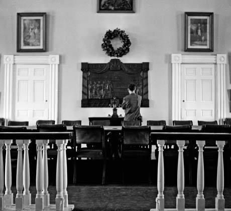 grayscale photograph: tourist reading wall plaque