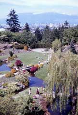 Color photo: Elevated view of Queen Elizabeth Park with Vancouver skyline as a distant backdrop