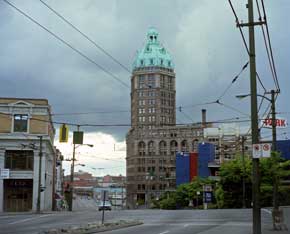 Color photo: Sun Tower building under dark clouds; bright patch of sky in distance