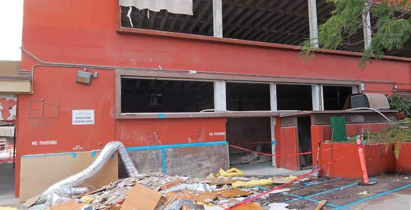 Debris in front of red building, bare ceiling rafters visable through removed windows