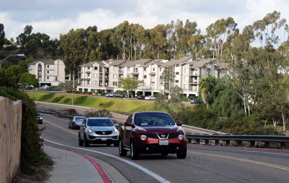 Two autos climbng hill with apartment  complex in background