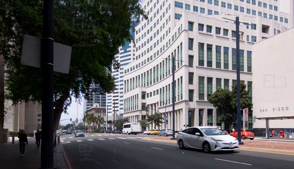 View down tree lined sidewalk with curve-faced Hall of Justice  building across street