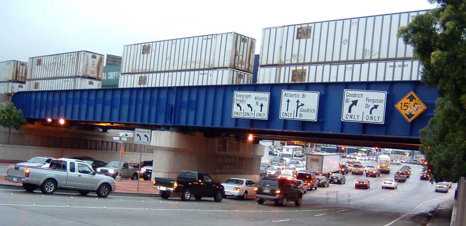 View of traffic passing under a railway bridge while double-stacked containers pass above
