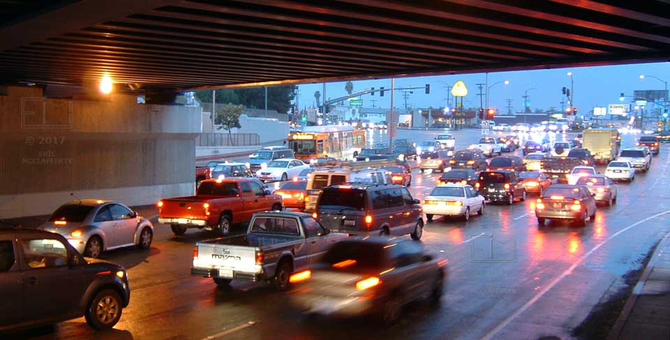View of traffic, in rain during twilight, from under railway overpass