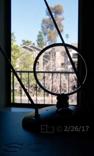 Color photo: Out fo focus view fron window with in fouus view of rabbit-ear attenna in foreground- Embedded text: 2/28/17