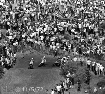 B/W photo: Overview of many spectators on hillsde observing racers negotiating turn in racetrack - Embedded text: 11/5/72