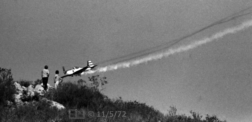 B/W photo: Stunt airplane appears close to spectators on nearby hill - Embedded text: 11/5/72