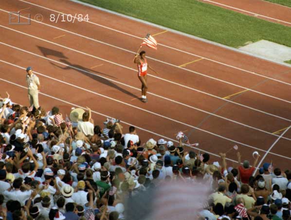 Color photo: An event winner, waving US flag, takes a victory lap  - Embedded text: 8/10/84