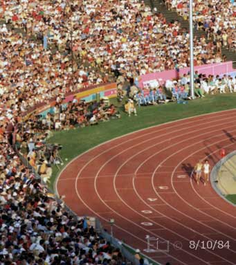 Color photo: Two runners race around curve side by side  - Embedded text: 8/10/84