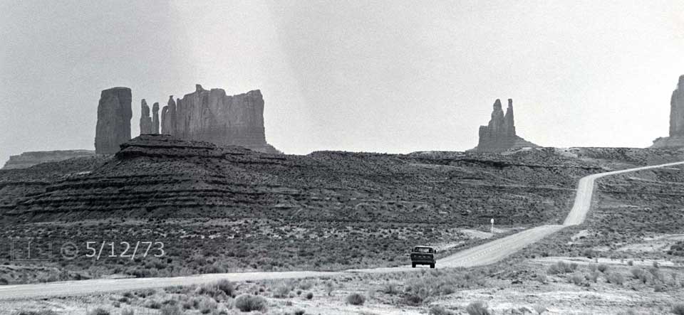 B/W photo: A highway through the desert with multiple buttes in the distance - Embedded text: 5/12/73