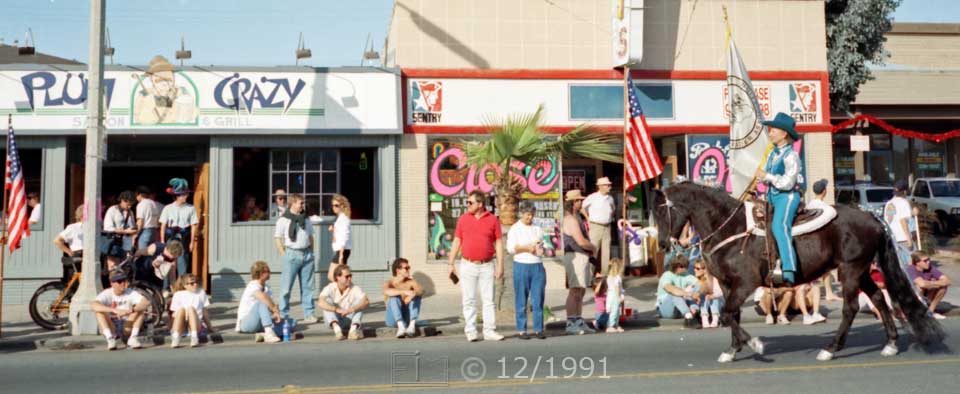 Color photo: Women on horse advances with spectators and Garnet St. store fronts in background - Embedded text: 12/1991