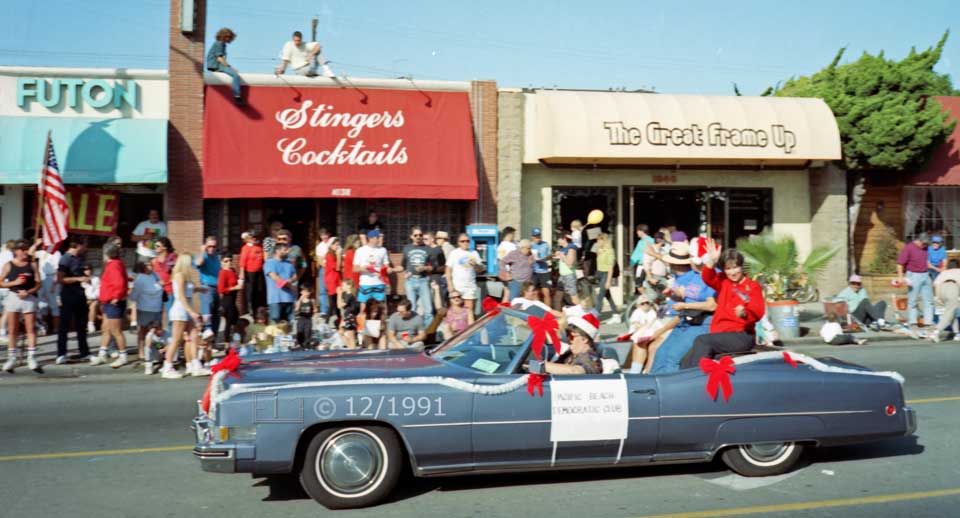 Color photo: Occupants of large convertible car wave to curbside and rooftop spectators - Embedded text: 7/20/91