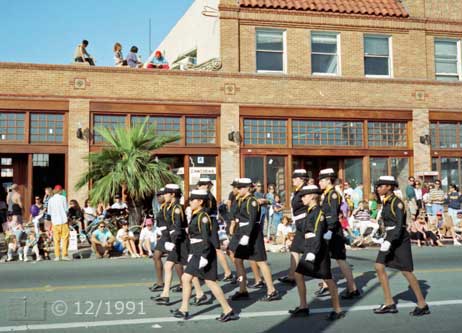 Color  photo: Female military marching in front of Dunaway Building being viewed from curbside and rooftop - Embedded text: 12/1991