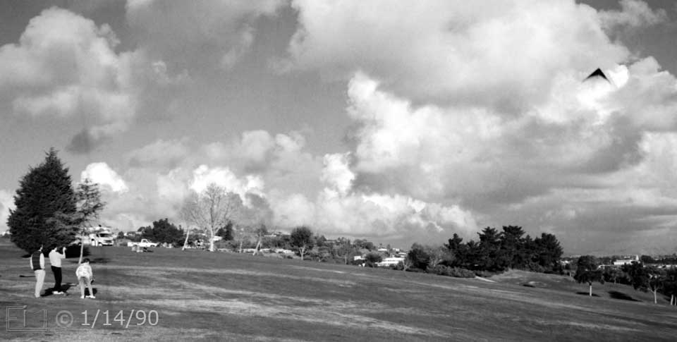 B/W photo: Kite flying in large, open area park - Embedded text: 1/14/90