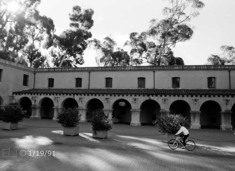 B/W photo: View of bicyclist cycling east on El Prado from steps of main entrance to Museum of Man/Us - Embedded text: 1/19/91