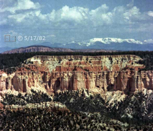 Color photo: Cliffs of eroded rock, forest and distant snow capped mountains - Embedded text: 5/17/82