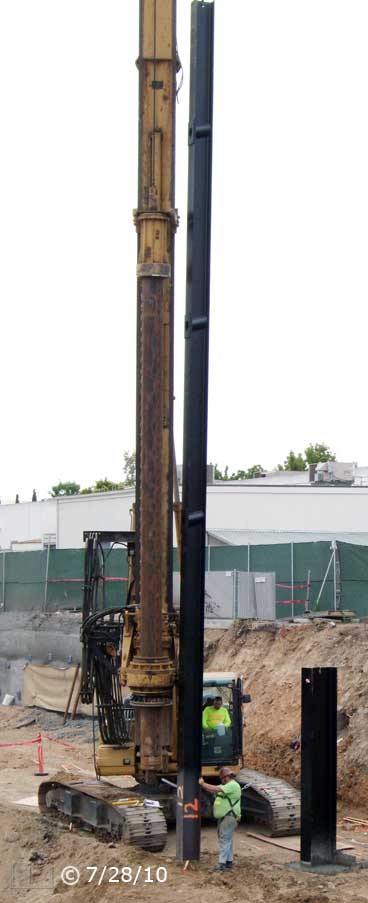 Color photo: Worker standing aside large I-beam vertically suspended from crane - Embedded text: 7/28/10