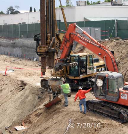 Color photo: Worker empting concrete bucket into I-beam post hole - Embedded text: 7/28/10
