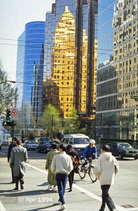 Color photo: Pedestrians, cyclist, traffic in foreground with older buildings refeced on glass walls of newer buildings in background - Image taken: 4/7~12/1994