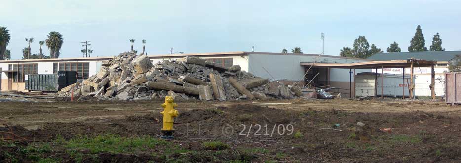 Color photo: Looking north-east across open field at rubble pile and old building - Embedded text: 2/21/09