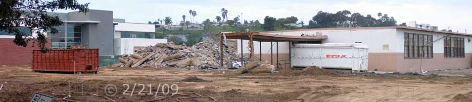Color photo: View across open field of new building, rubble pile and old building - Embedded text: 2/21/09