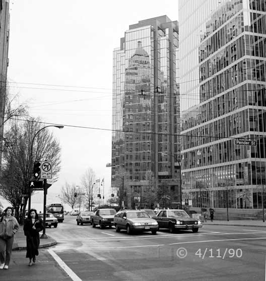 B/W photo: Vancouver street scene with reflection of Marine Building on glass wall of a nearby high-rise - Embedded text: 4/11/90