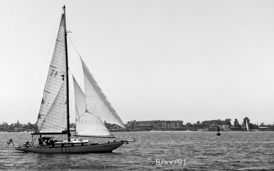 B/W photo: A boat under sail with Coronado shore in background - Embedded text: 8/xx/91