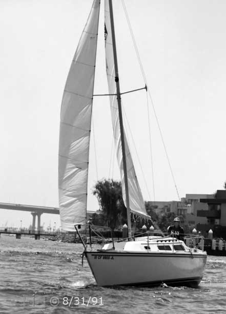 B/W photo: Port-bow view of boat under sail with Coronado Bridge and Coronado in background - Embedded text: 8/31/91