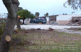 Color photo: View of base slab and rubble of demolished building and to be demolished buildings beyond
